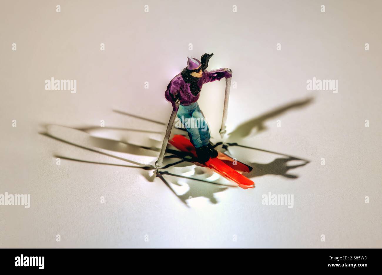 Figurine miniature d'un homme qui skine sur la neige d'hiver sur des skis rouges colorés entourés de multiples ombres et recopie Banque D'Images