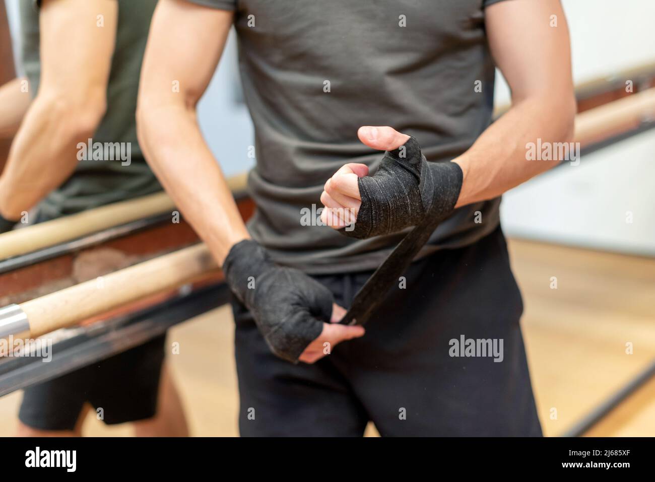 Mise au point douce d'un sportif méconnaissable en casque d'activité enveloppant les bandages noirs autour de la main et du poignet tout en se tenant près du miroir au début du travail de boxe Banque D'Images