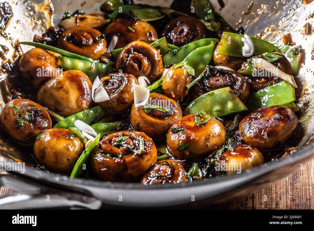 Champignons rôtis dans un wok avec petits pois, oignons et sauce teriyaky. Banque D'Images