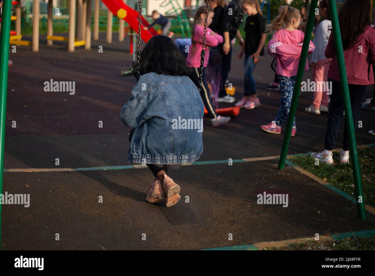 Fille sur swing. Adolescent sur l'aire de jeux. Cheveux noirs et jeans bleus sur la jeune fille. Une écolière prend une pause pour étudier dans la cour. Balançoire à corde pour enfants Banque D'Images