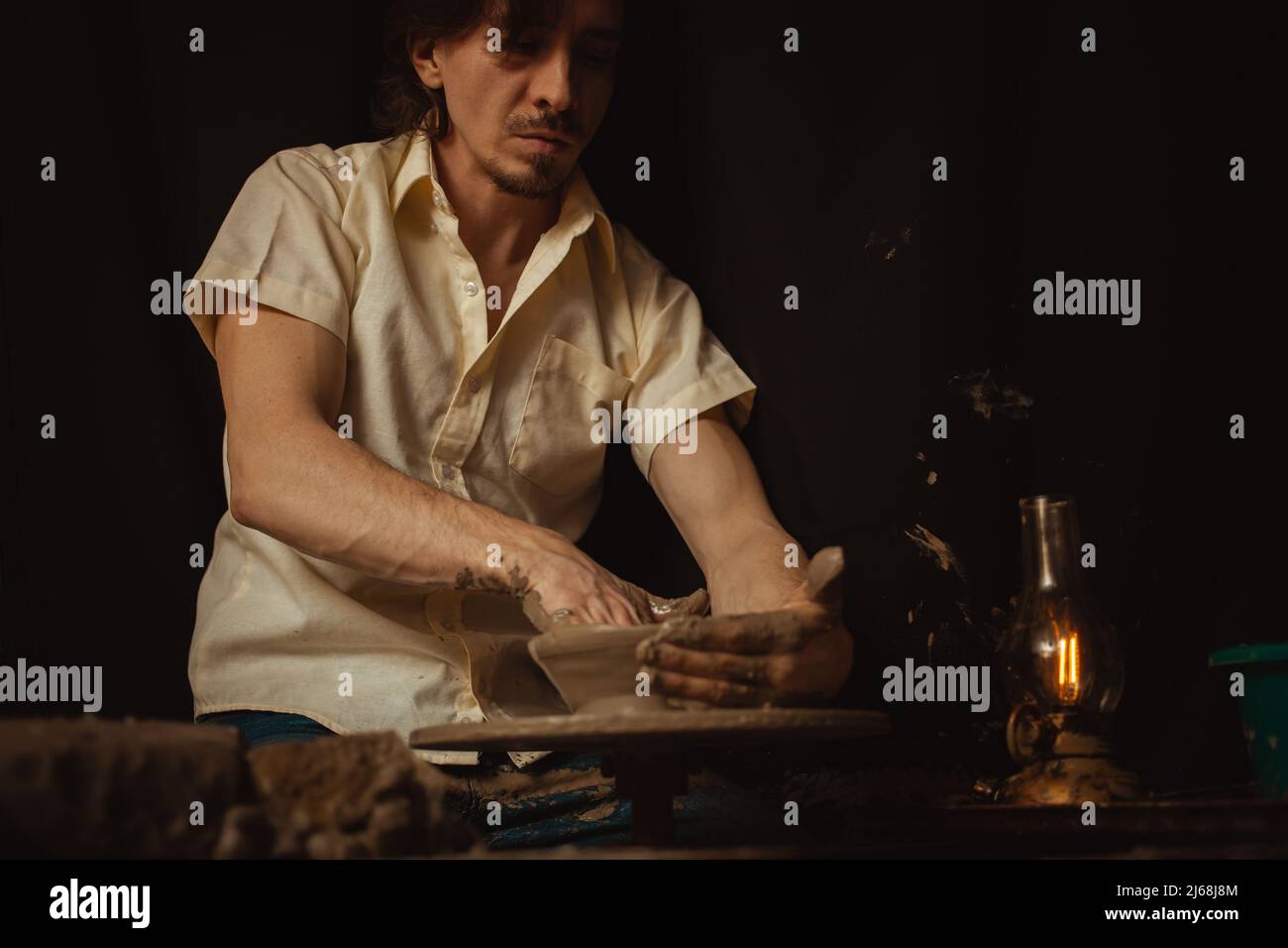 homme dans atelier de poterie fait plaque d'argile, une atmosphère authentique, lampe jaune, style de vie, atmosphère magique. Concept avec vos propres mains, maison fr Banque D'Images