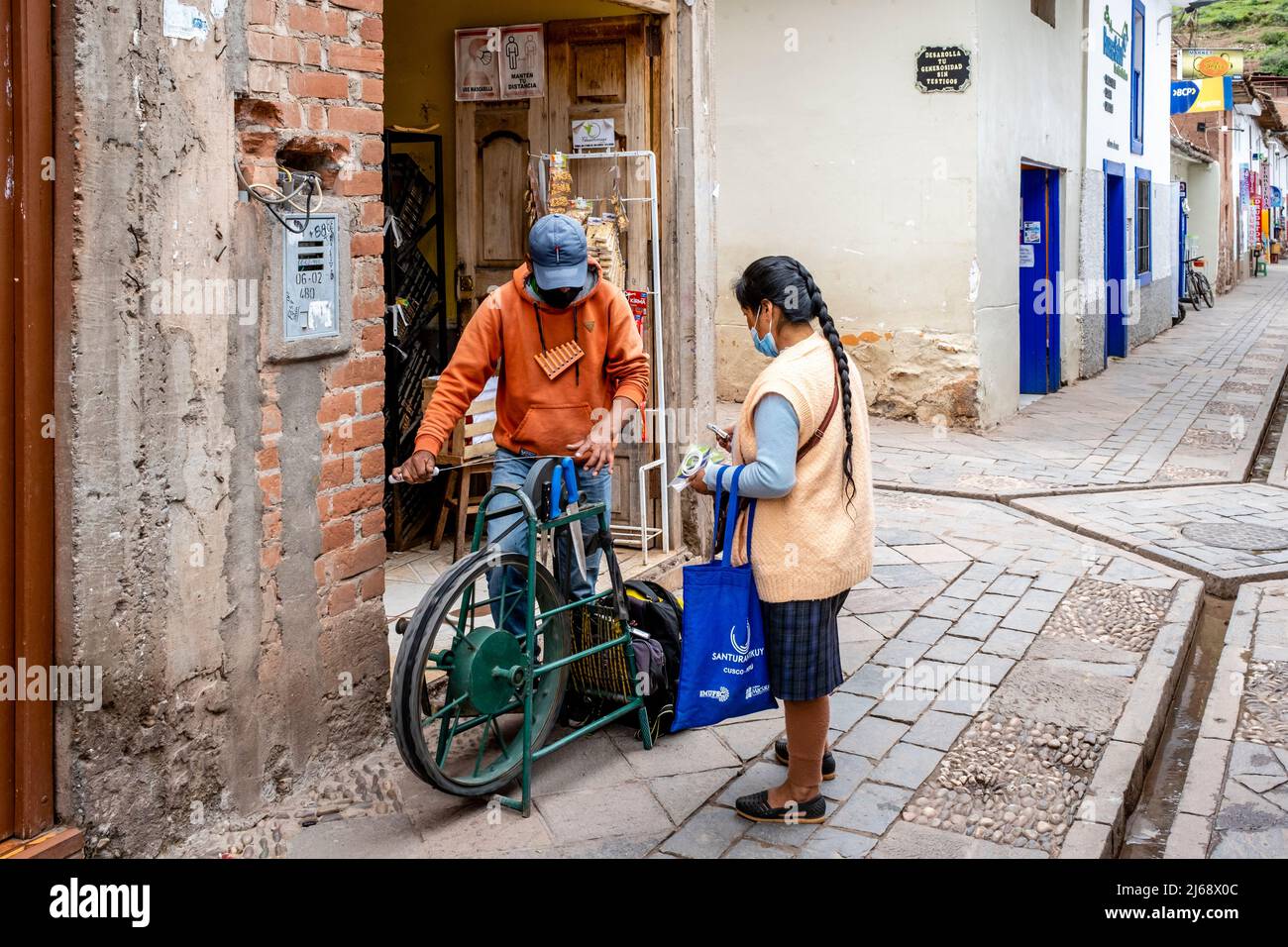 Un jeune homme aiguise des couteaux dans la rue à l'aide d'un ancien vélo aiguiseur de couteau, Pisac, la vallée sacrée, province de Calca, Pérou. Banque D'Images