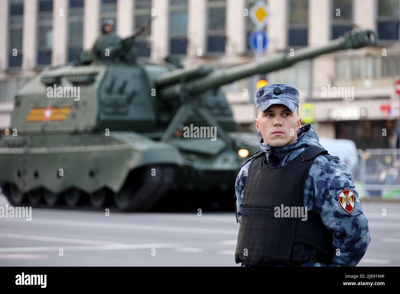 Soldat des forces militaires russes de la Garde nationale debout sur fond d'artillerie automotrice 2S19 'Msta-s' Banque D'Images