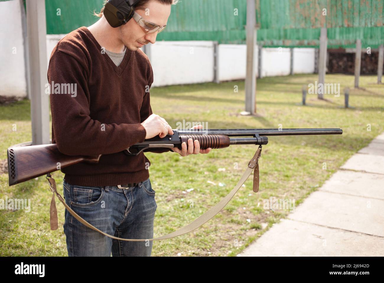 Un jeune homme charge un fusil à pompe avec un Ammo. calibre 12. Pneu extérieur. Un homme dans un casque et des lunettes se prépare à tirer. Armes à feu pour le tir sportif, passe-temps. Banque D'Images