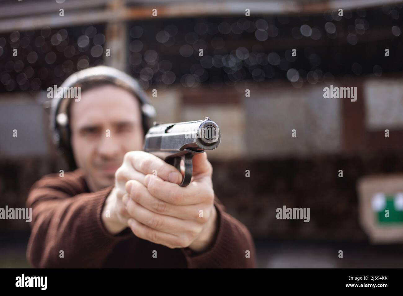 Un jeune homme tire un fusil, visant la cible. Un homme portant un casque de protection. Un mur et un toit avec trous de balle. Champ de prise de vue en extérieur Banque D'Images