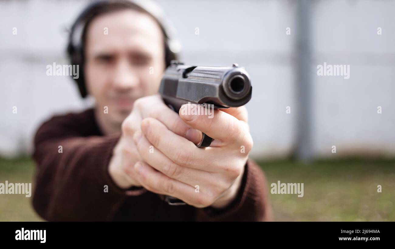 Un jeune homme cherche un fusil. Un homme portant un casque de protection. Gamme de tir de pneu extérieur. Hobby. Arme à feu contre le mur blanc Banque D'Images