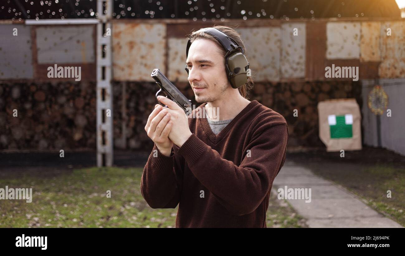 Un jeune homme tire un fusil, visant la cible. Un homme portant un casque de protection. Un mur et un toit avec trous de balle. Champ de prise de vue en extérieur Banque D'Images