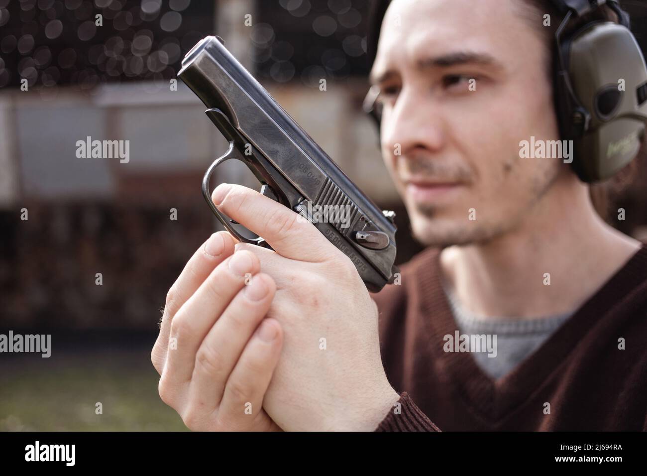 Un jeune homme tire un fusil, visant la cible. Un homme portant un casque de protection. Un mur et un toit avec trous de balle. Copie de plage de prise de vue en extérieur Banque D'Images