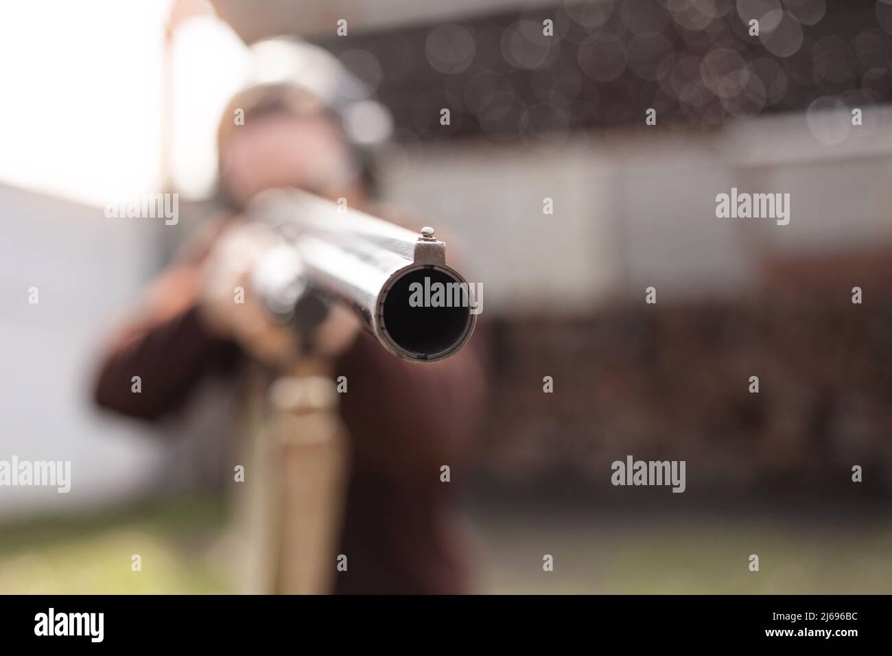 Un jeune homme dans des lunettes de protection et des écouteurs. Un fusil à pompe. Pneus à l'extérieur. Un mur et un toit avec trous de balle. Espace de copie sport Banque D'Images