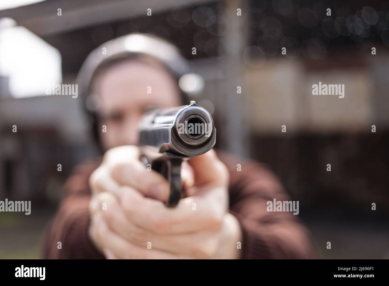 Un jeune homme tire un fusil, visant la cible. Un homme portant un casque de protection. Un mur et un toit avec trous de balle. Champ de prise de vue en extérieur Banque D'Images