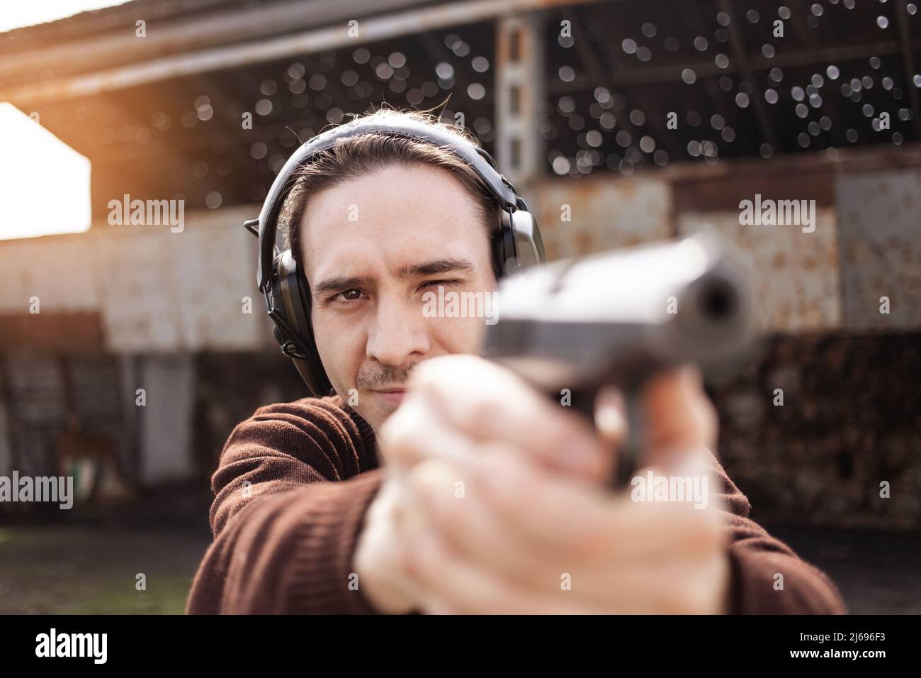 Un jeune homme tire un fusil, visant la cible. Un homme portant un casque de protection. Un mur et un toit avec trous pour balles. Champ de prise de vue en extérieur en gros plan Banque D'Images