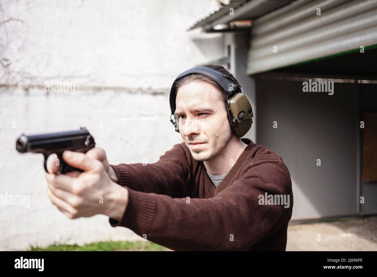 Un jeune homme cherche un fusil. Un homme portant un casque de protection. Gamme de tir de pneu extérieur. Hobby. Arme à feu contre le mur blanc Banque D'Images