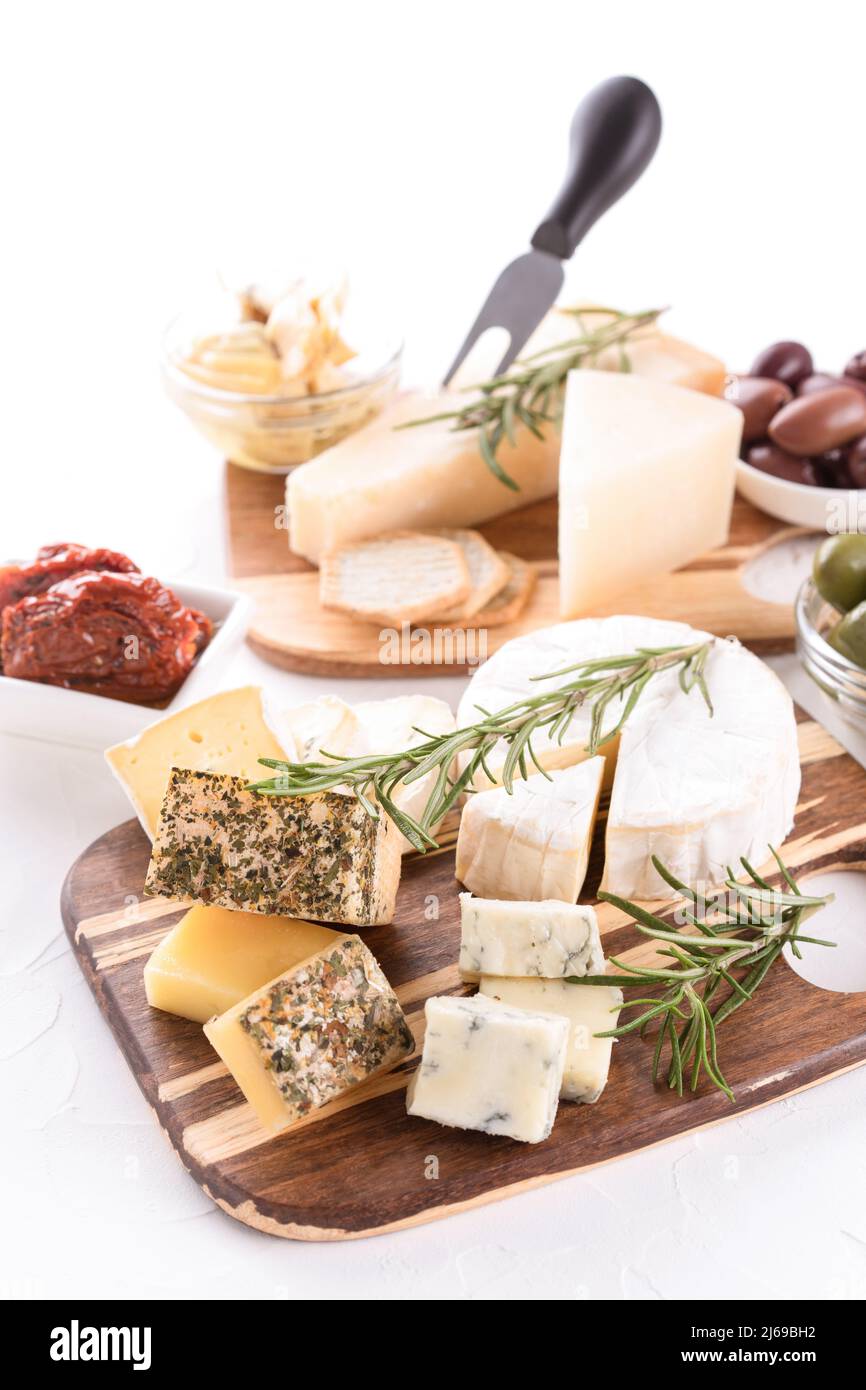 Plateau de fromages en bois avec sélection de fromages servis avec des olives et des tomates séchées sur table blanche. Assiette de fromages avec des fromages artisanaux pour un Banque D'Images