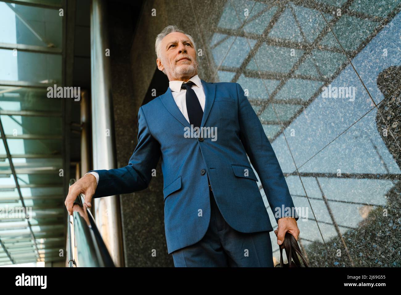 Homme gris senior habillé en costume descendant les escaliers à l'extérieur Banque D'Images