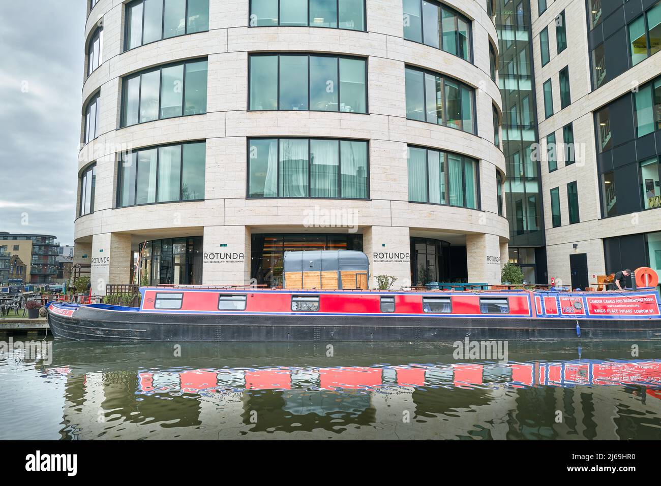 Un long canal et étroit bateau garé sur le canal Regents à côté du restaurant Rotunda dans le bâtiment Kings place près de Kings Cross, Londres, Angleterre. Banque D'Images