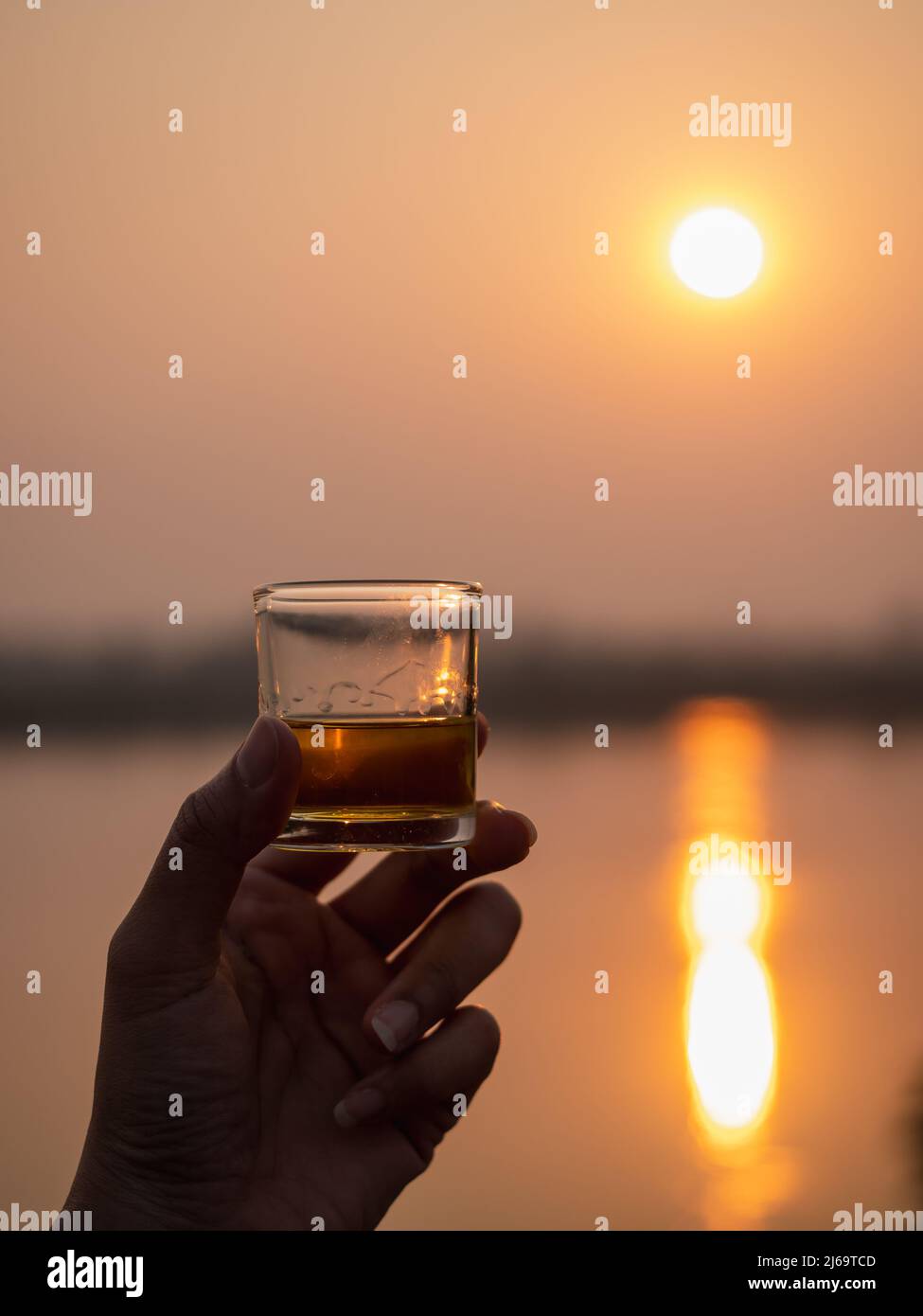 Une photo de whisky à la main sur fond de coucher de soleil et de rivière. Banque D'Images