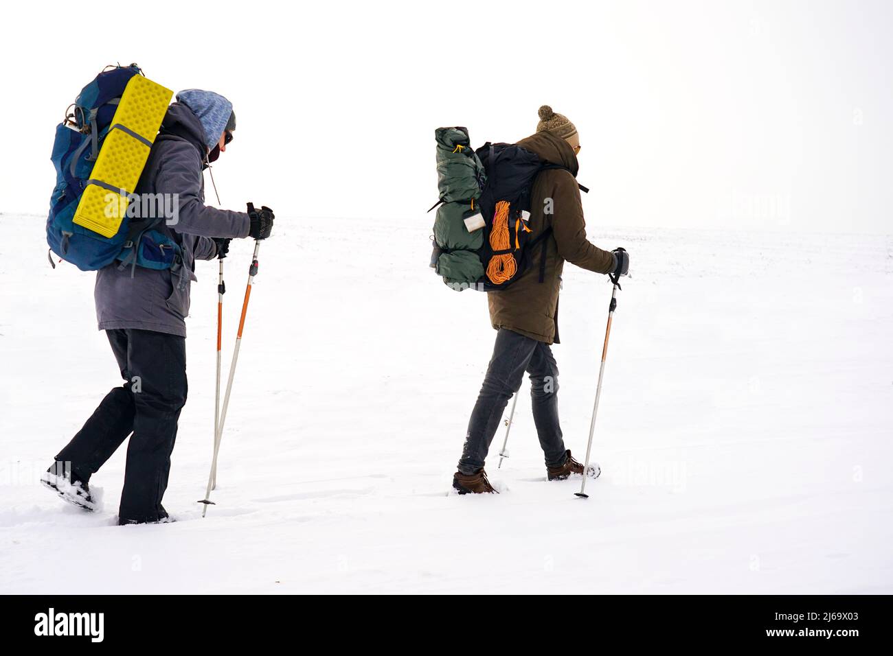 Deux gars marchent dans la neige au cours d'une expédition d'hiver. Ils portent de grands sacs à dos et des vestes chaudes. Ils tiennent des bâtons de randonnée dans leurs mains. Banque D'Images