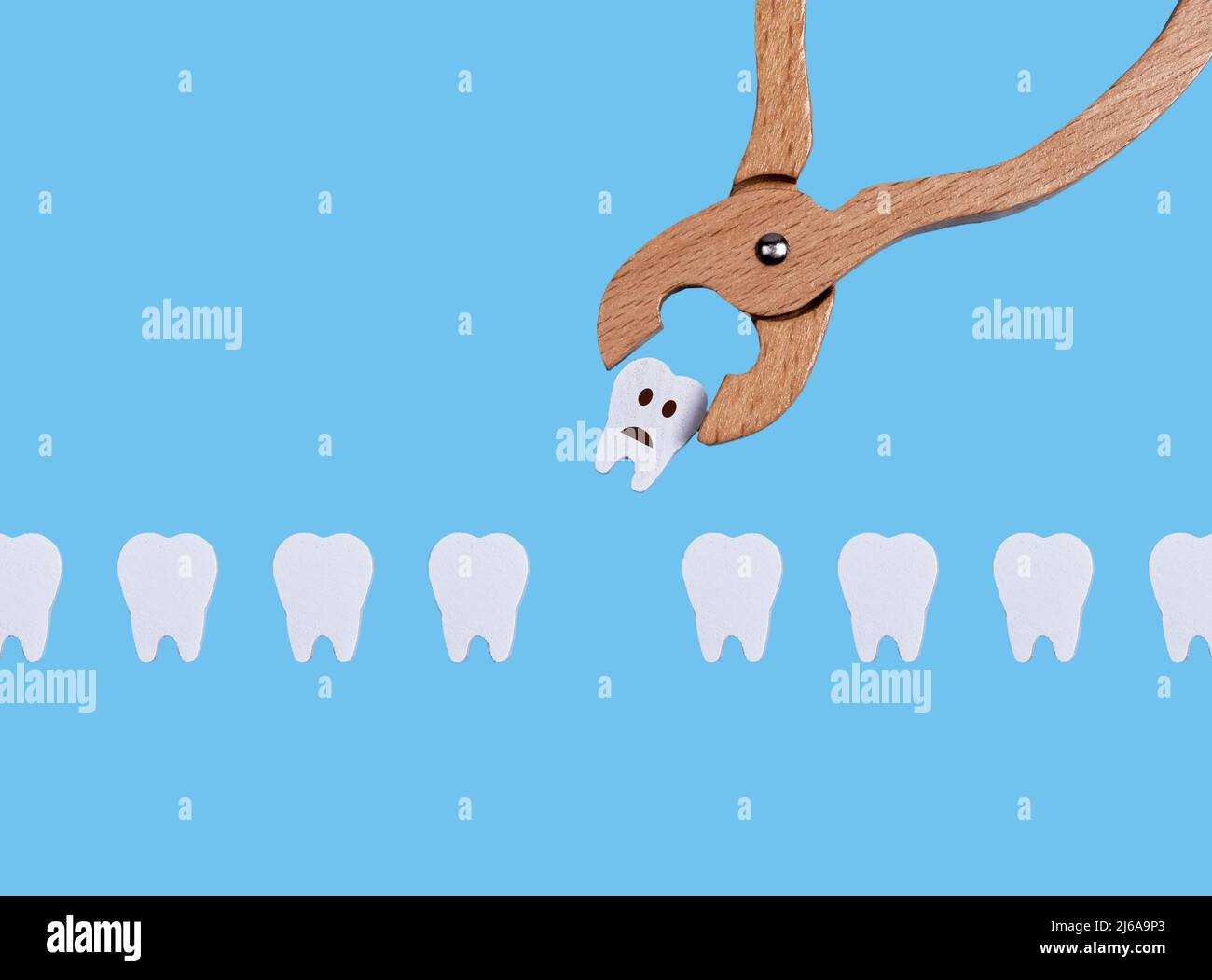 Rangée de dents et pinces dentaires. Tirer la mauvaise dent malade avec un emoji triste en raison de la carie, maladie parodontale. Concept de santé bucco-dentaire et de travail chez le dentiste sur fond bleu. Jeu d'enfants chez le médecin. Photo Banque D'Images