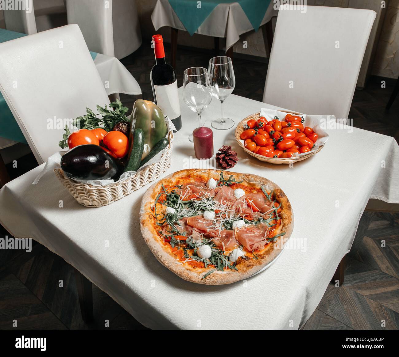 Table servie dans un restaurant pizzeria avec pizza, tomates et un panier de légumes frais, verres à vin et une bouteille de vin, photo de stock, restaurant Banque D'Images
