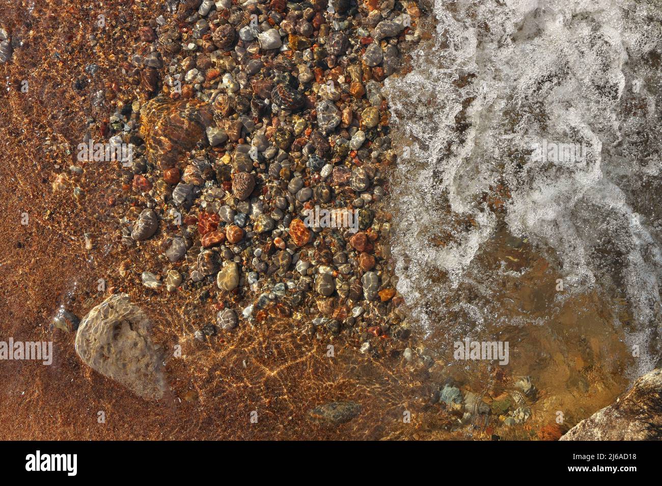 Petites vagues qui se roulent dans Sandy Beach parsemées de galets, rochers et pierres colorés Banque D'Images