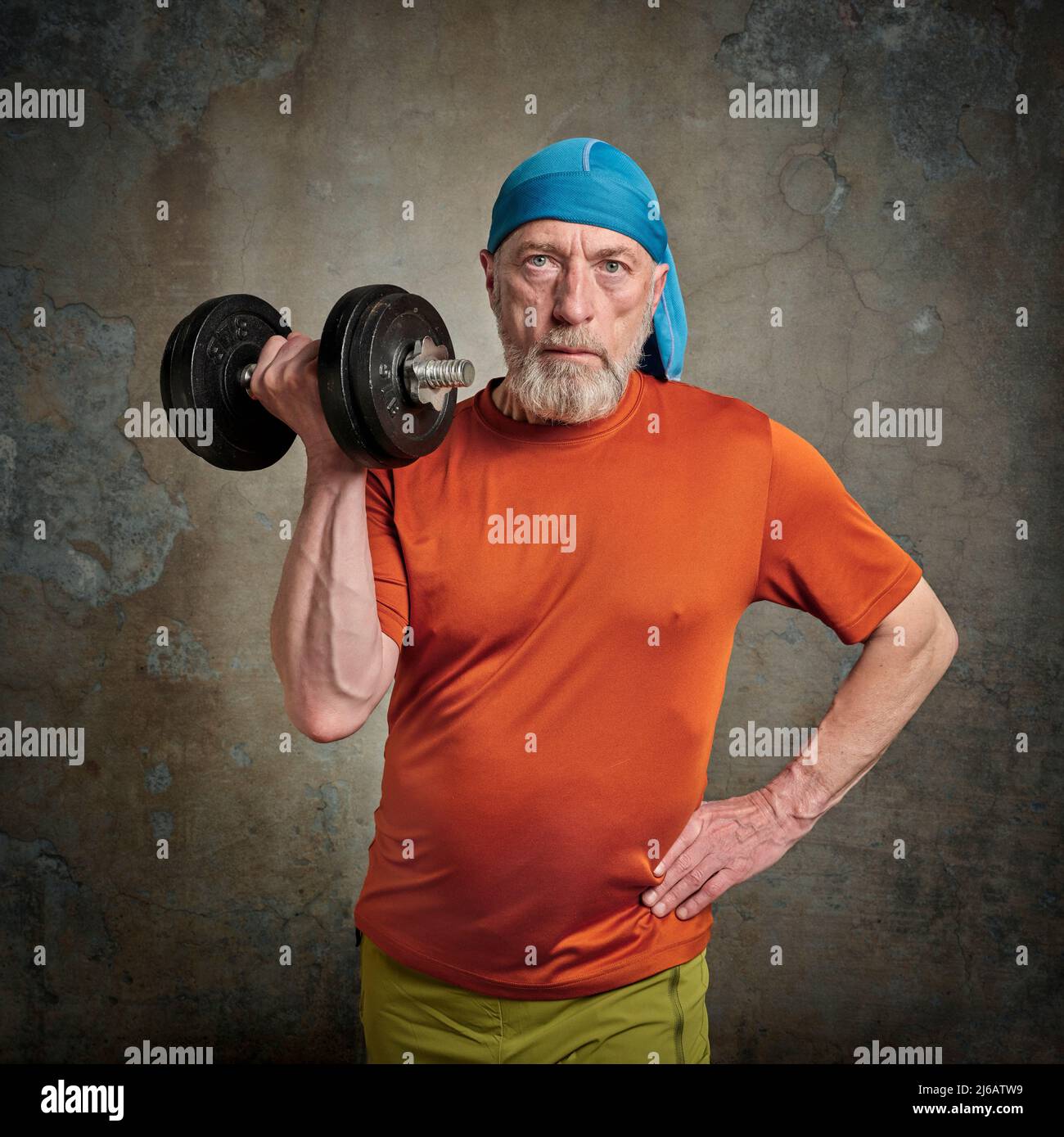 portrait décontracté d'un vieil homme barbu (fin 60s) en train d'exercer avec une lourde haltères, un senior actif et un concept de fitness, grunge fond urbain Banque D'Images