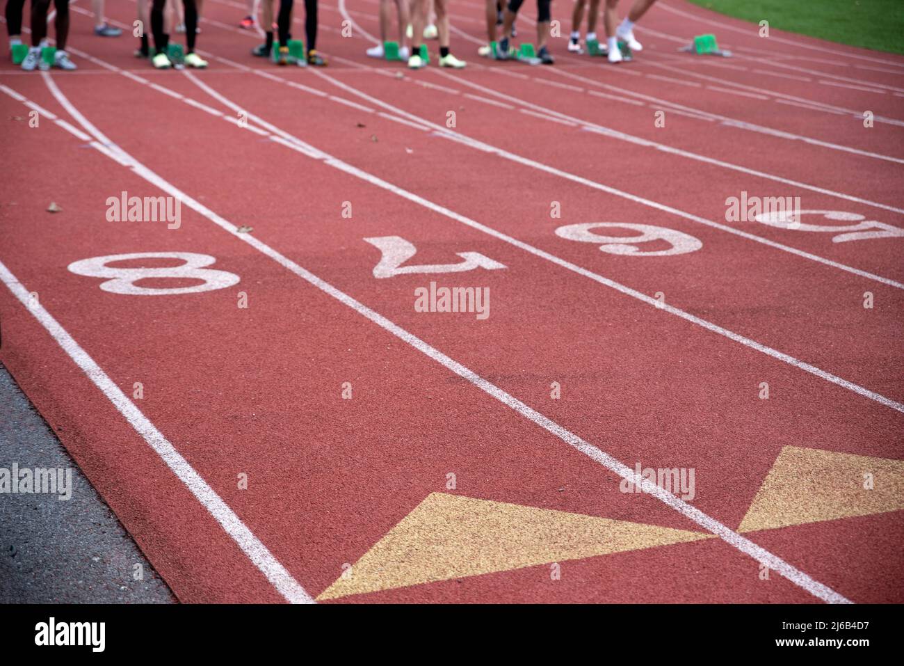 Les coureurs sont en place sur la ligne de départ sur une piste de course sportive, en gros plan avec des marquages et des chiffres filés à l'extérieur avec un espace de copie. Banque D'Images