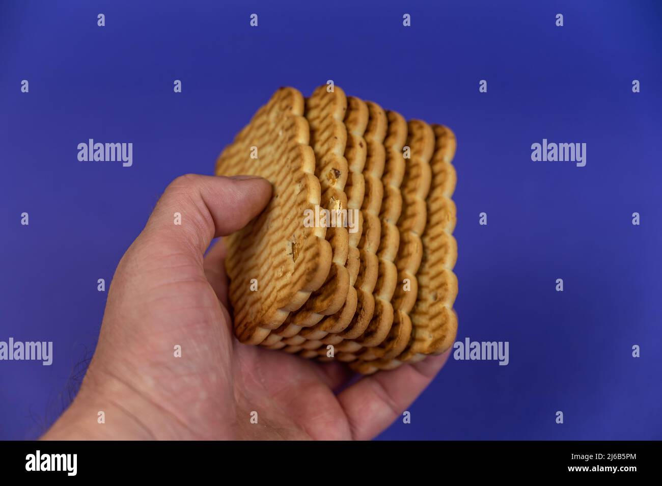 Une main tient une pile de biscuits rectangulaires sur fond bleu. Gâteries prêtes à manger avec arachides dans la main de l'homme. Banque D'Images