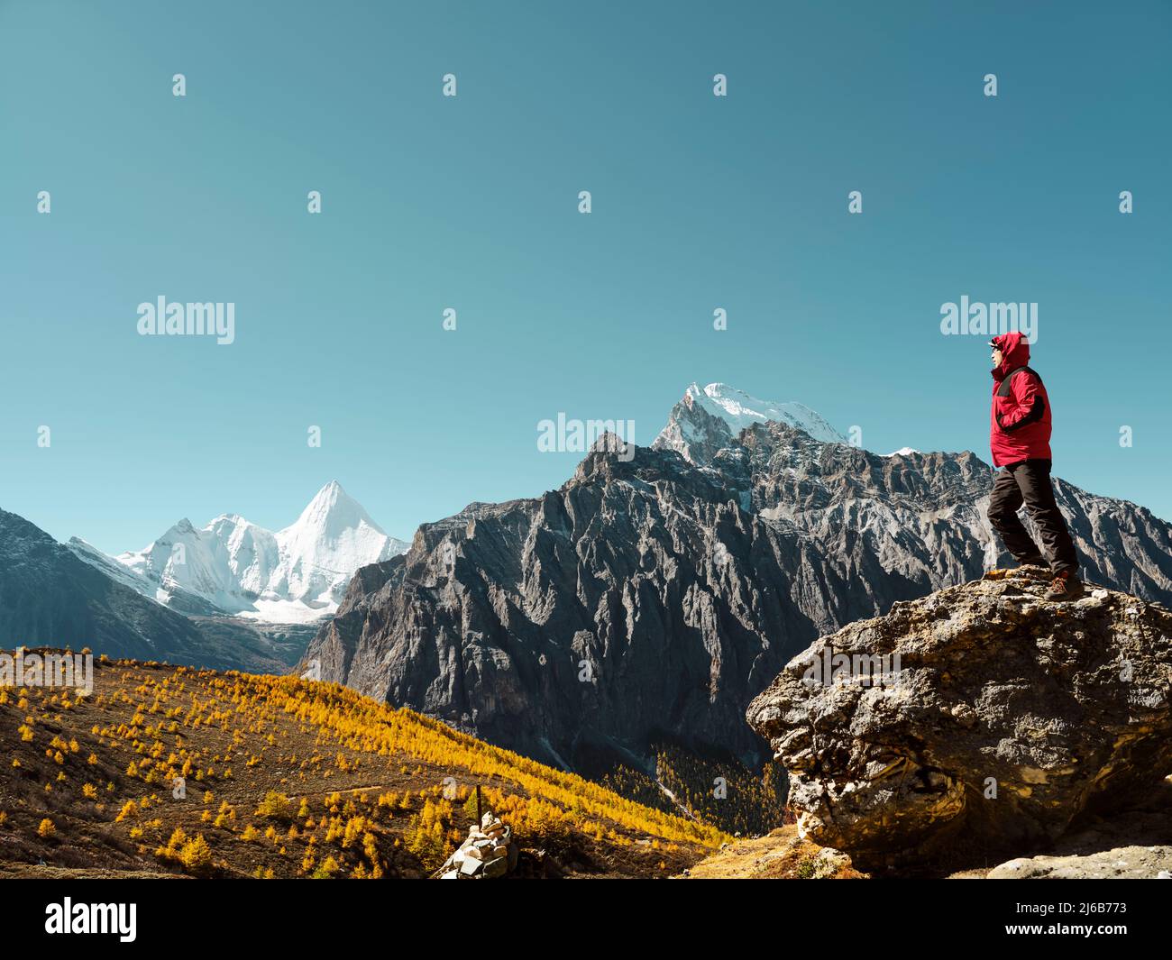 Homme asiatique debout sur le rocher regardant le sommet de la montagne de Yangmaiyong (ou Jampayang en tibétain) au loin à Yading, dans le comté de Daocheng, dans le Sichuan Banque D'Images