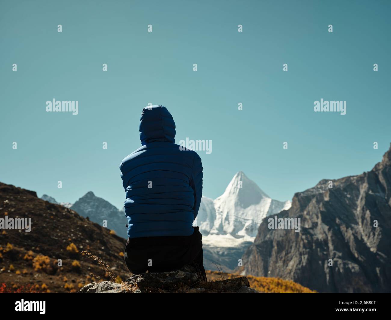 Vue arrière d'une femme asiatique assise au-dessus d'une montagne voisine qui donne sur le mont Yangmaiyong (ou Jampayang en tibétain) à Yading, dans le comté de Daocheng, dans le Sichua Banque D'Images