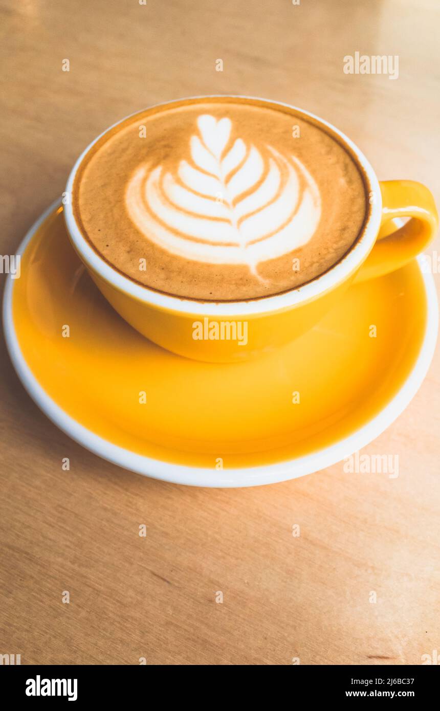 Tasse de cappuccino jaune en céramique avec latte art se dresse sur une table en bois, photo verticale en gros plan Banque D'Images