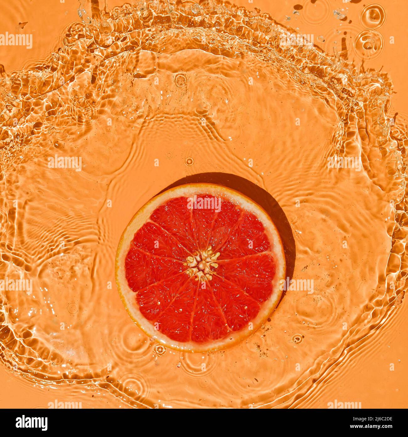 Fruit d'été concept pamplemousse rouge citronné sur fond orange vif avec des éclaboussures de mouvement d'eau. Banque D'Images