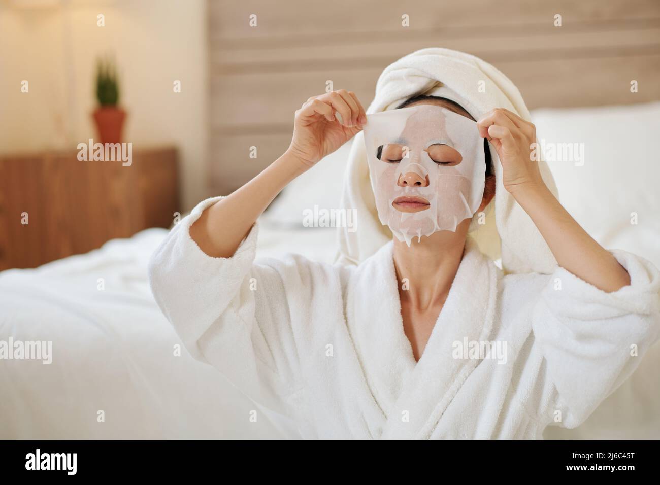 Yougn femme en peignoir enlever masque de feuille hydratant Banque D'Images