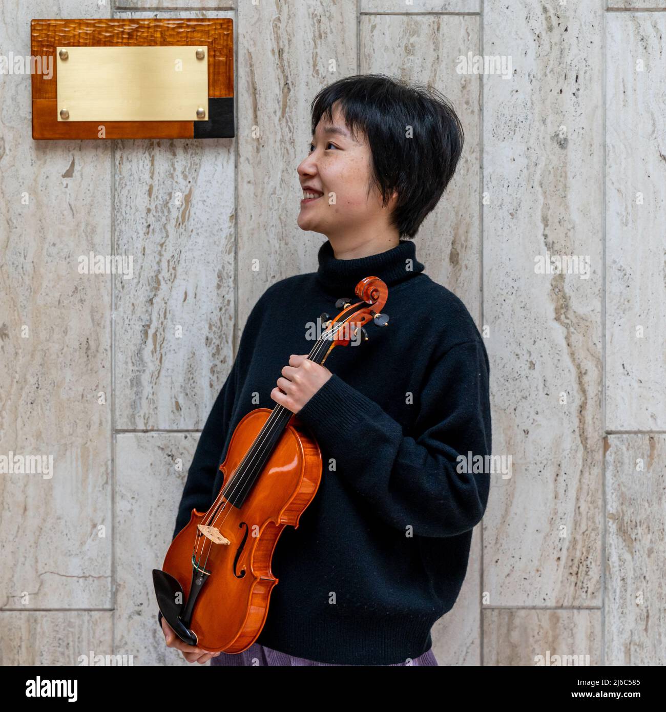 Jeune violoniste chinoise montrant son violon fraîchement préparé à l'extérieur devant son atelier Banque D'Images