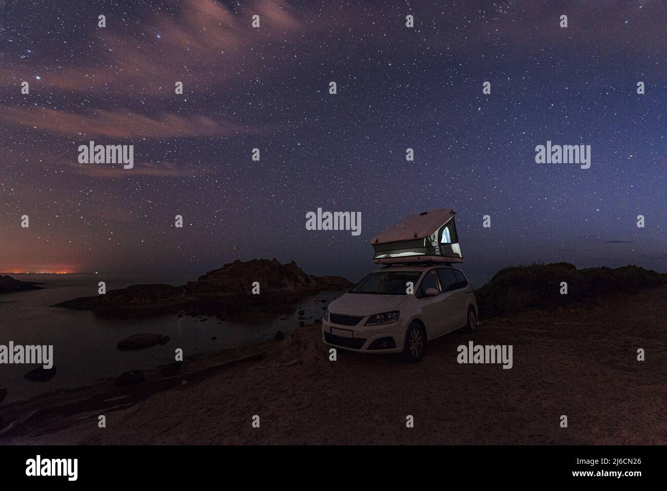 Camping Vanlife à la mer - minibus avec tente sur le toit au bord d'une baie sur la côte ouest de la Sardaigne sous le ciel étoilé brillant, Italie, Europe Banque D'Images