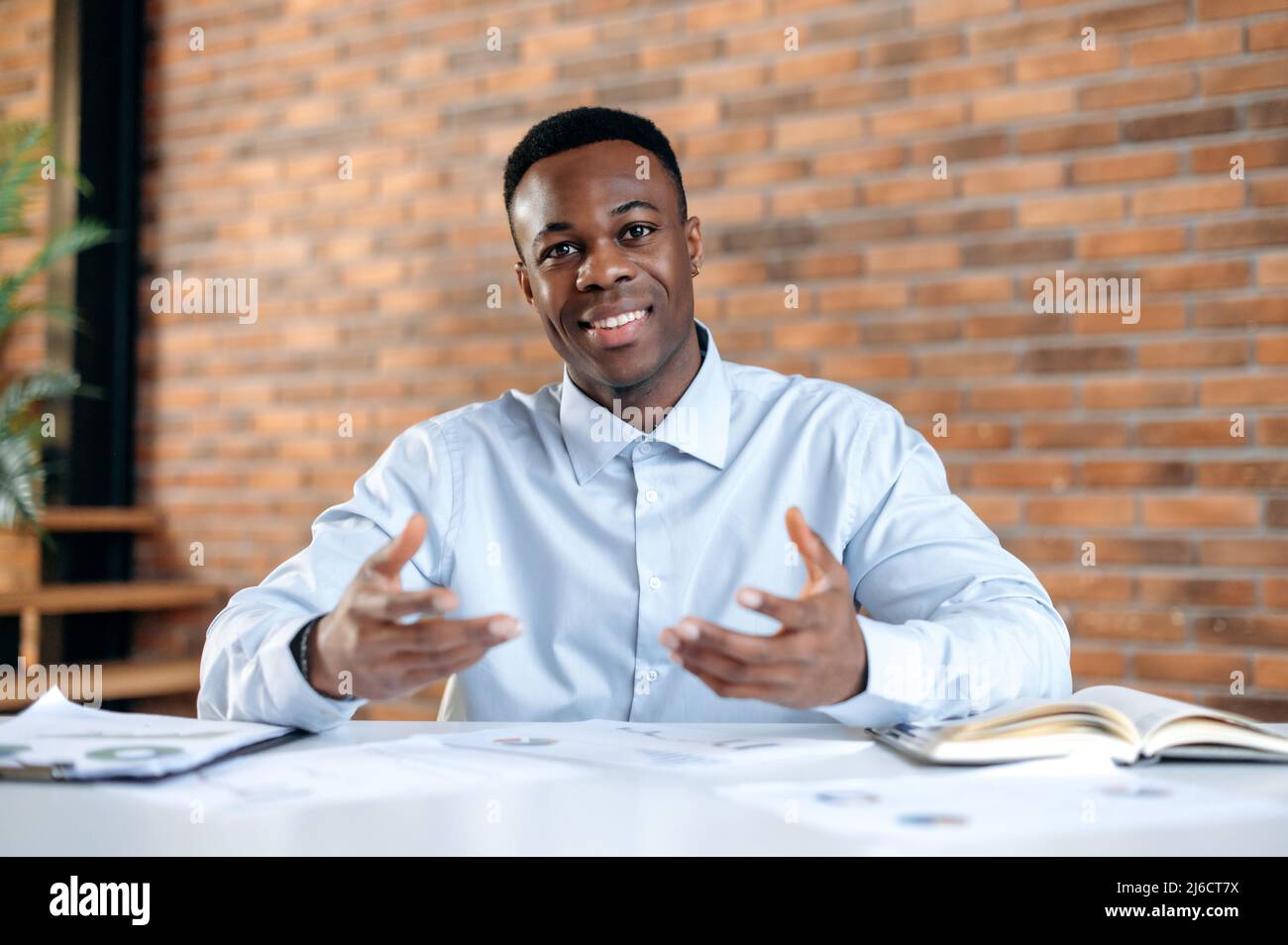 Un dirigeant d'entreprise afro-américain, un mentor ou un responsable d'entreprise séduisant et réussi s'entretient avec un employé ou un client lors d'une communication vidéo, d'un brainstorming, d'un gestuelle avec les mains, d'un coup d'œil à la caméra, d'un sourire Banque D'Images