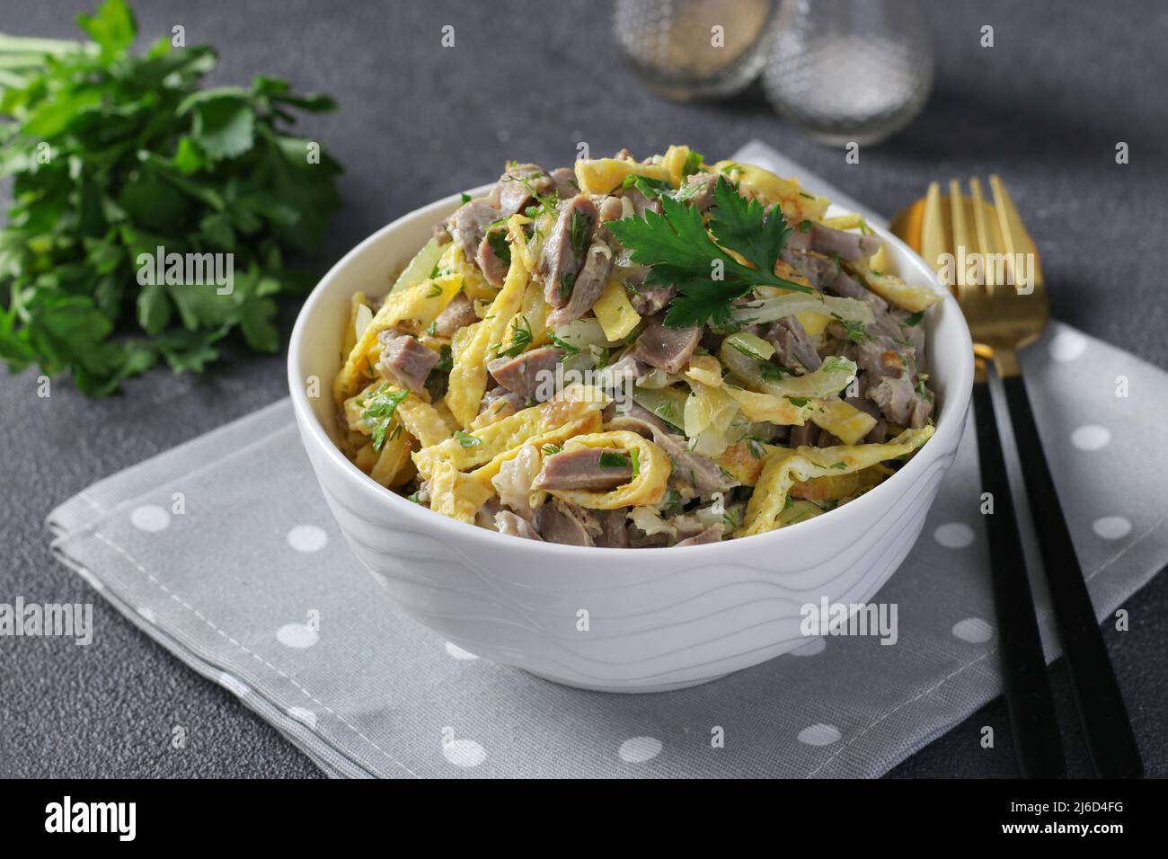 Salade avec stomachs de poulet, crêpes brouillés et oignons frits dans un bol blanc sur fond gris foncé Banque D'Images