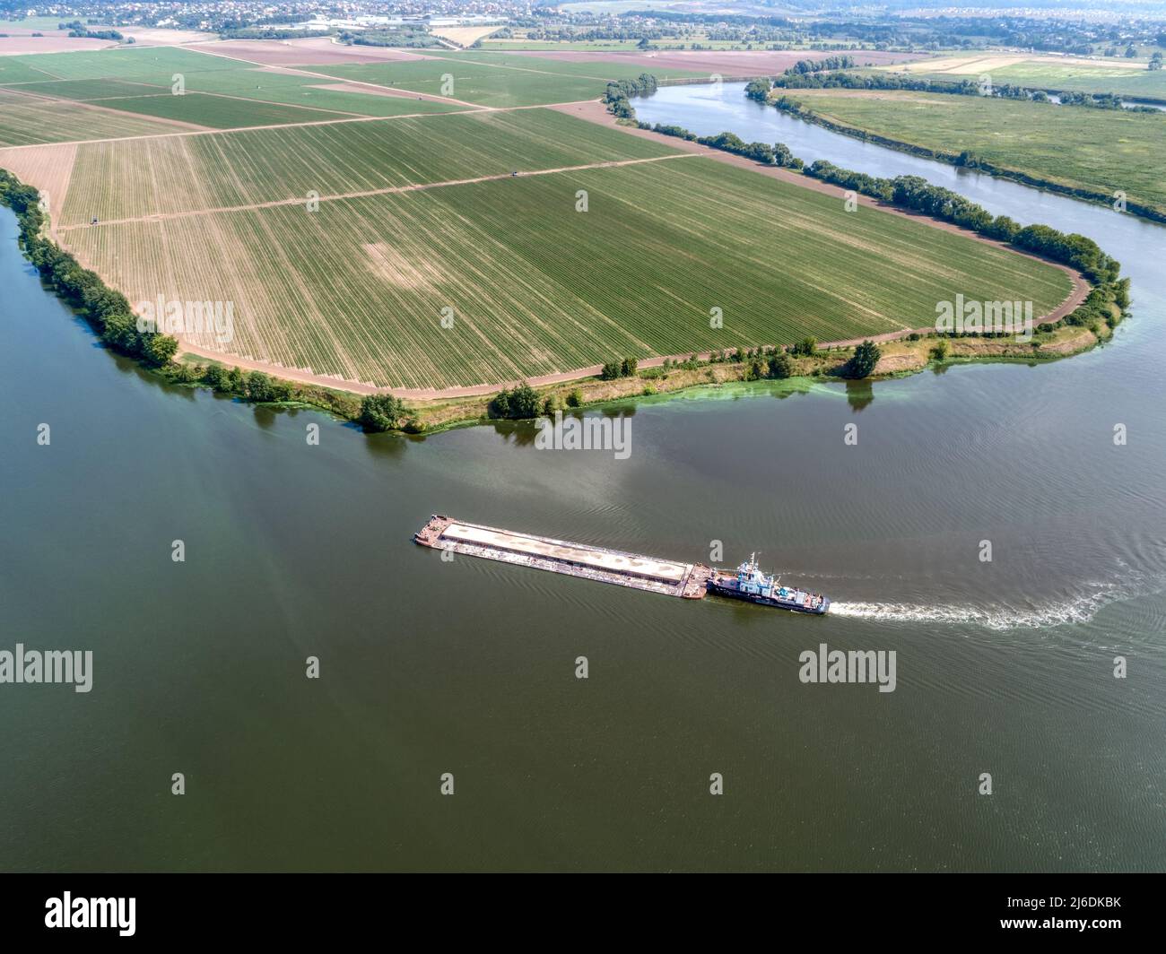 Un petit remorqueur pousse la barge le long de l'eau calme au-delà des champs Banque D'Images