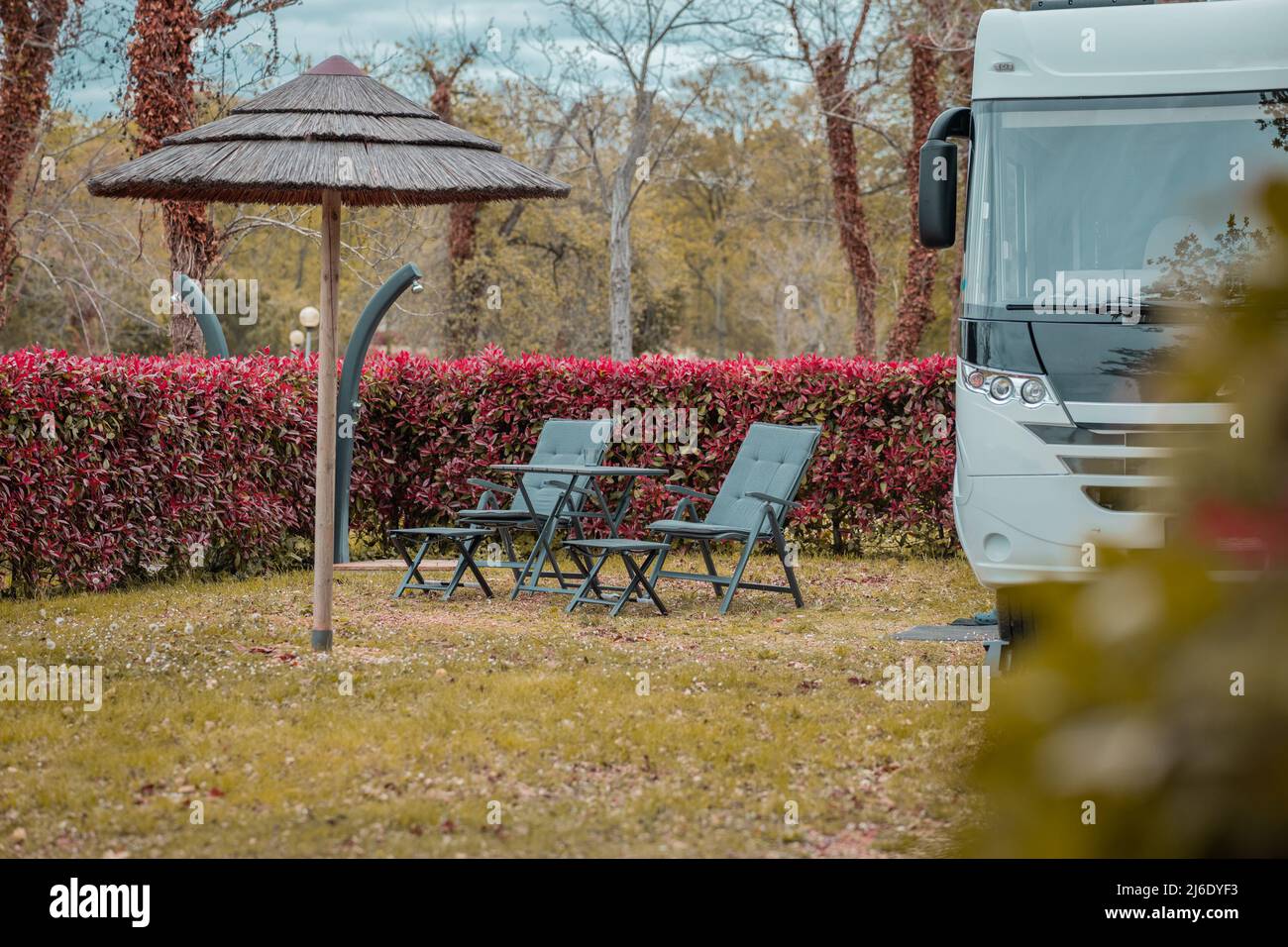 Deux chaises longues vides devant un motard chic et moderne, garés dans un joli camping-car entouré de plantes rouges luxuriantes. Camping moderne avec caméra Banque D'Images