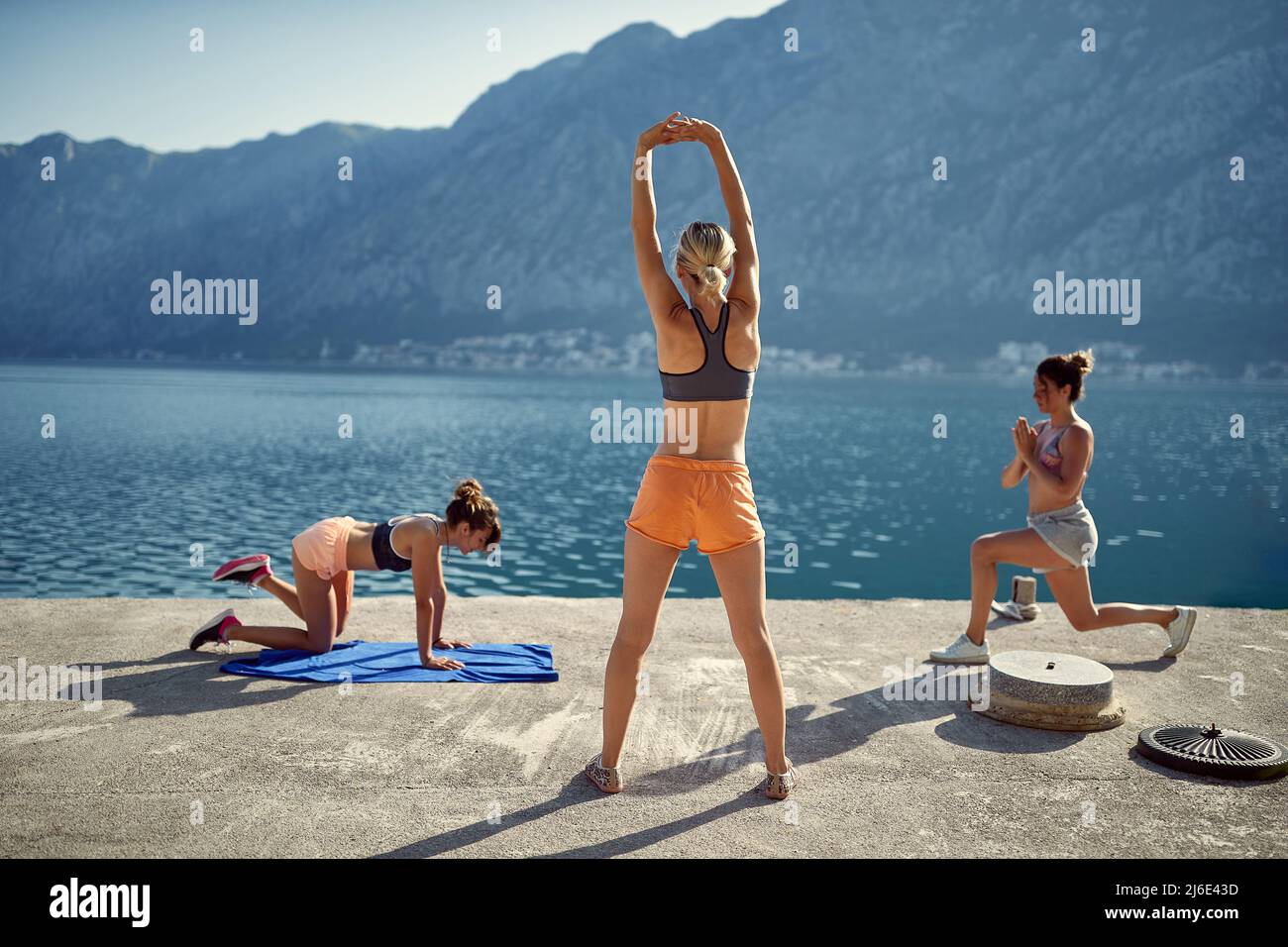 Trois femmes s'exercent à l'extérieur, près de l'eau. Stretching, yoga, concept de loisirs. Banque D'Images