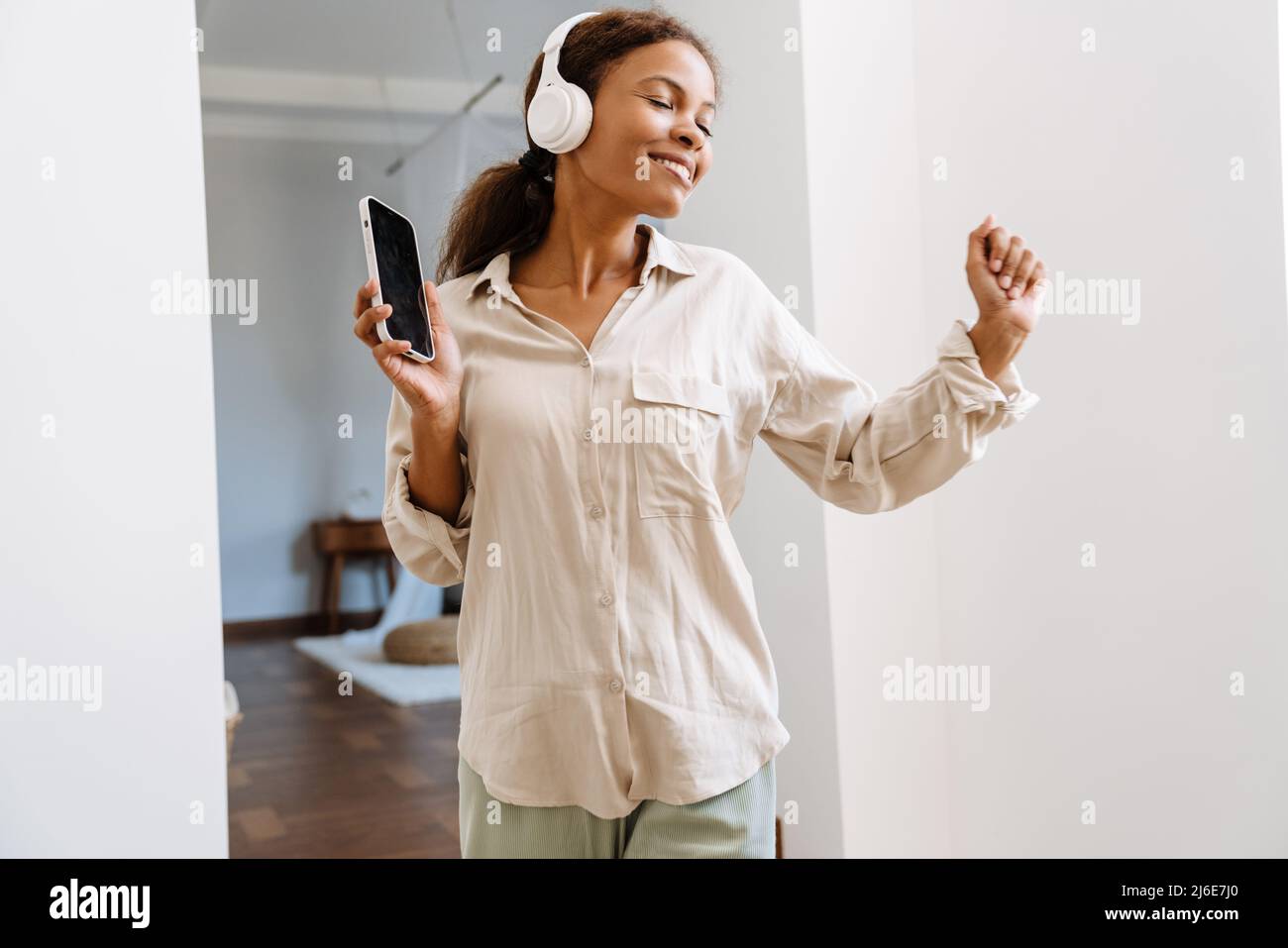 Jeune femme noire dansant et souriant tout en écoutant de la musique à la maison Banque D'Images