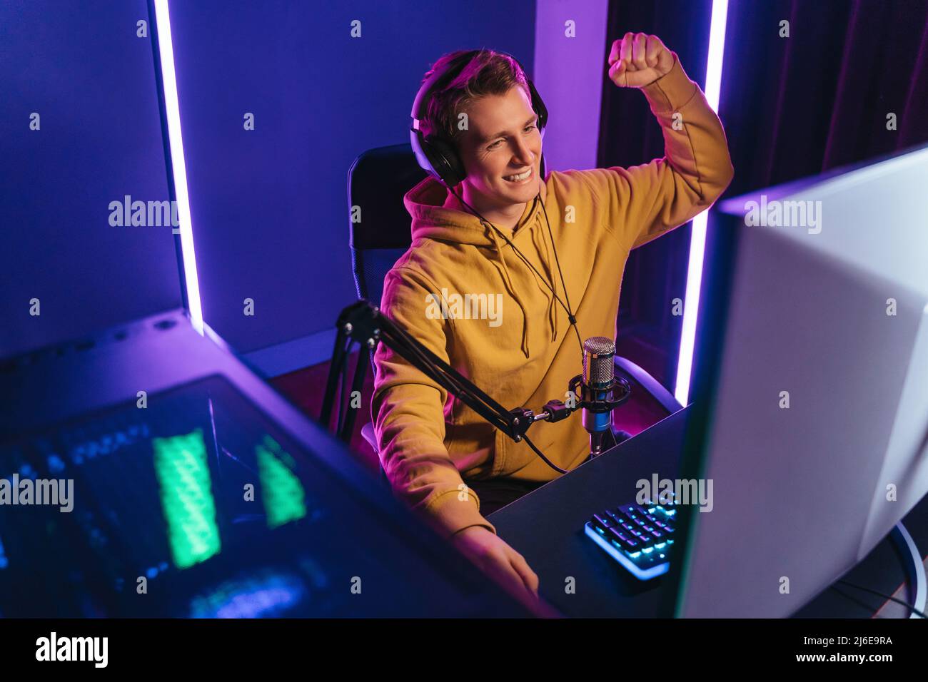 Jeune joueur professionnel souriant de cybersport streaming tout en jouant au jeu de tir sur PC à la maison, levant le bras, a gagné le tournoi esport. Les cyber-sportifs aiment Banque D'Images