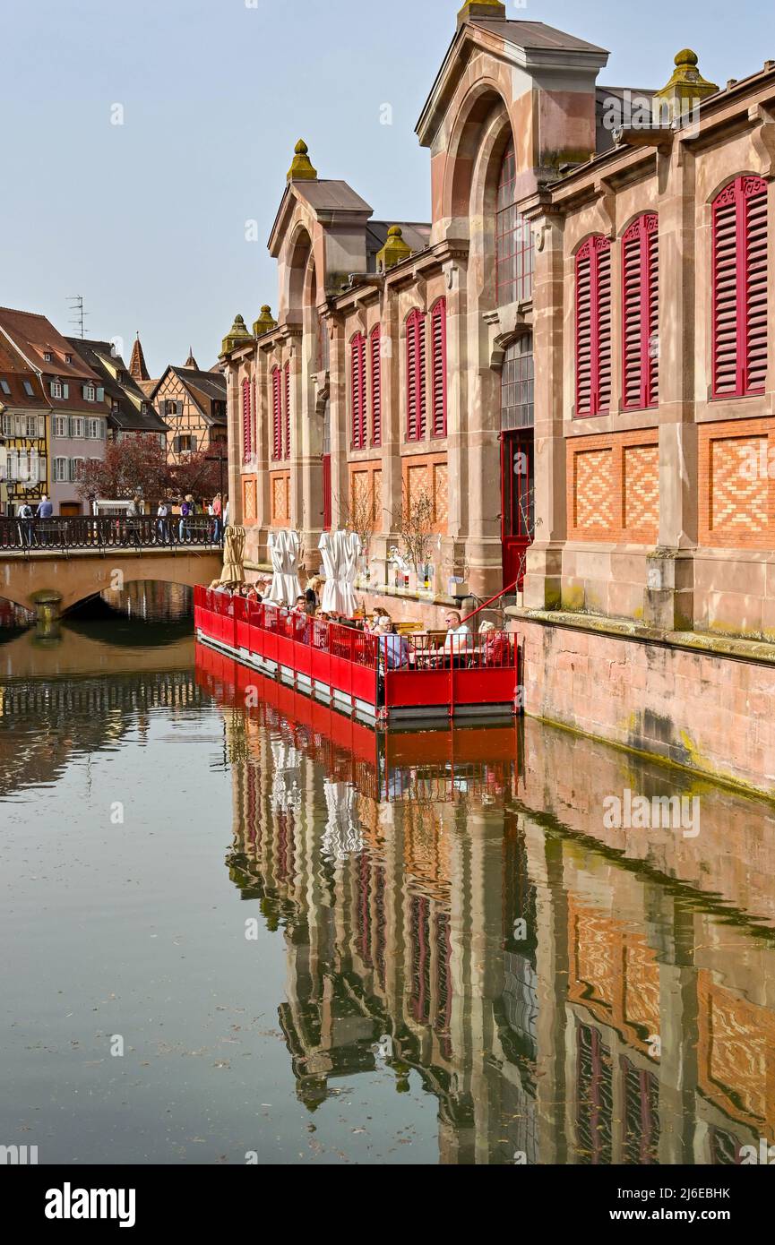 Colmar, France - avril 2022 : personnes assises aux tables d'un café sur un ponton flottant sur le canal à l'extérieur du bâtiment du marché Banque D'Images
