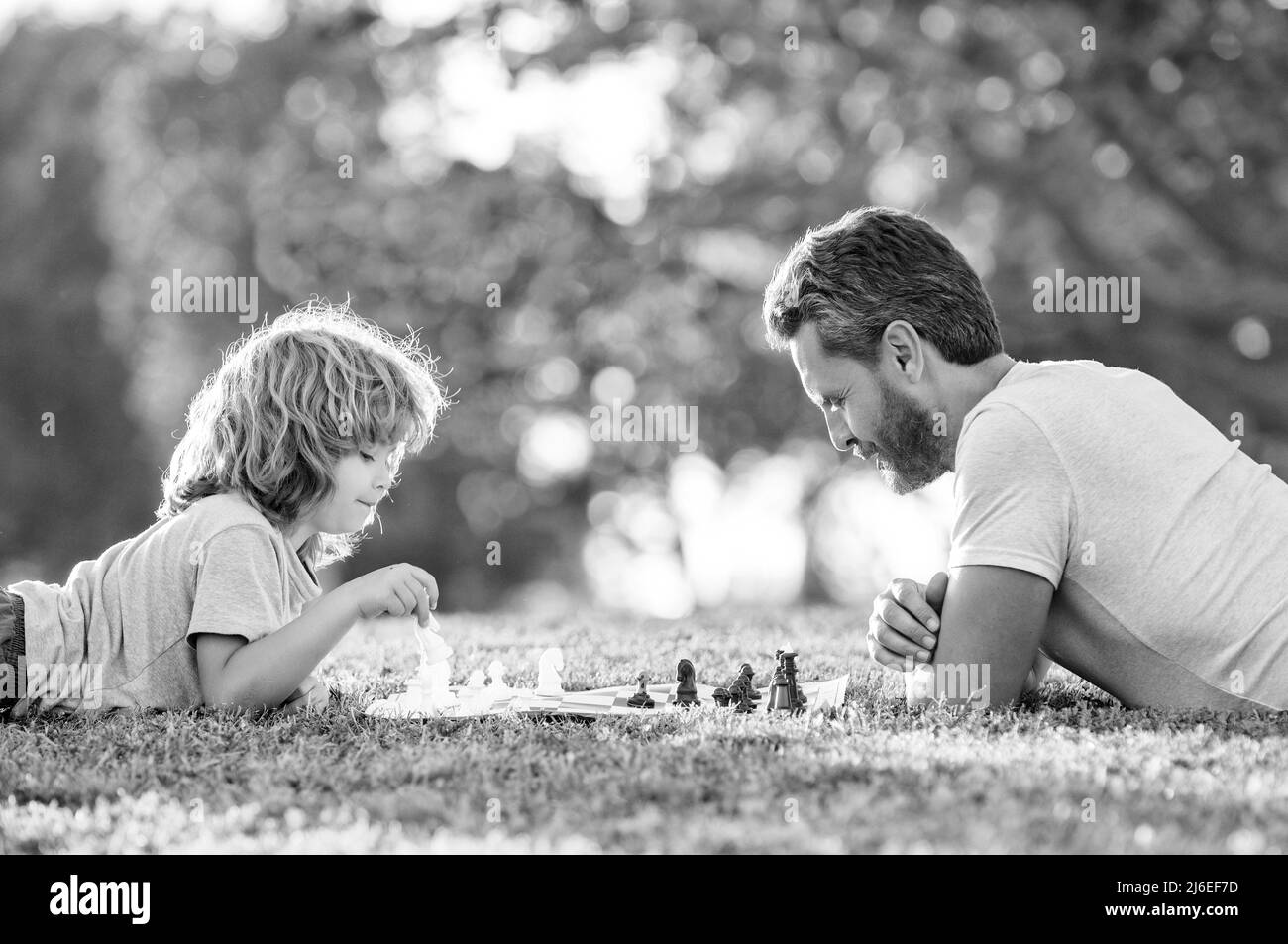 famille heureuse de père homme et fils enfant jouant aux échecs sur l'herbe verte dans le parc extérieur, paternité Banque D'Images