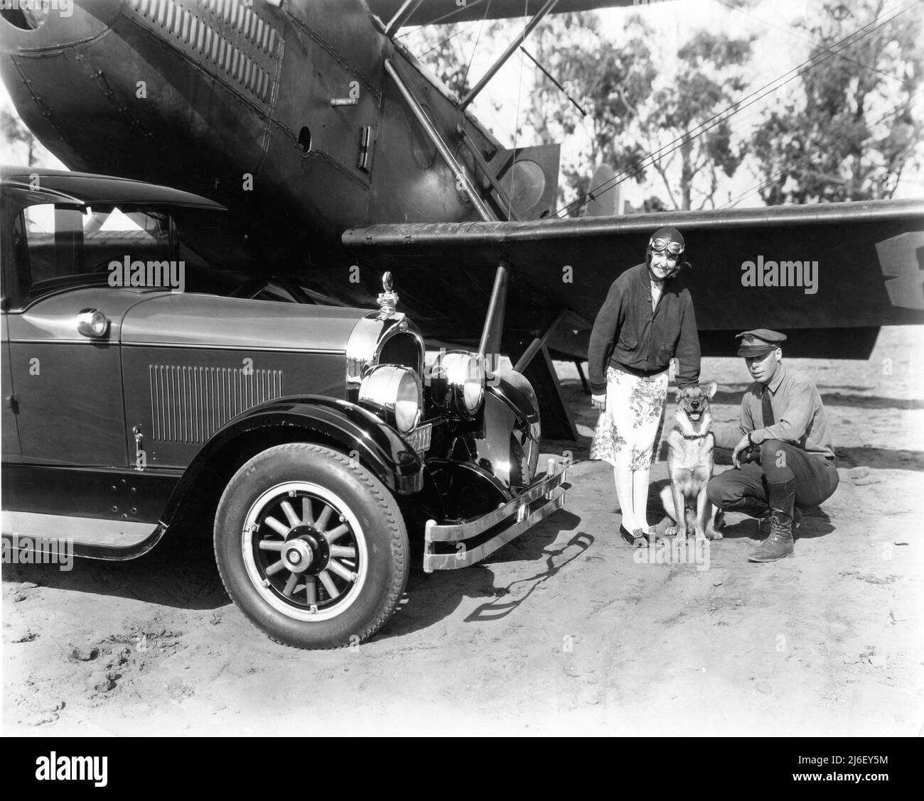 L'actrice de film silencieuse HAZEL KEENER à l'aérodrome militaire de Californie pose avec chien et officier militaire à côté de Bi-plane et Automobilecirca 1925 Banque D'Images