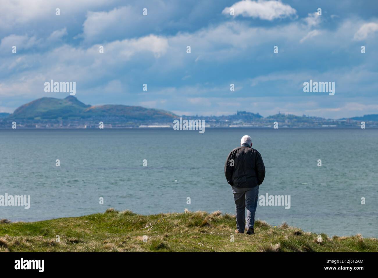 Un homme plus âgé marchant sur Firth of Forth Coast avec vue sur Arthur's Seat et la ville d'Édimbourg au loin, East Lothian, Écosse, Royaume-Uni Banque D'Images