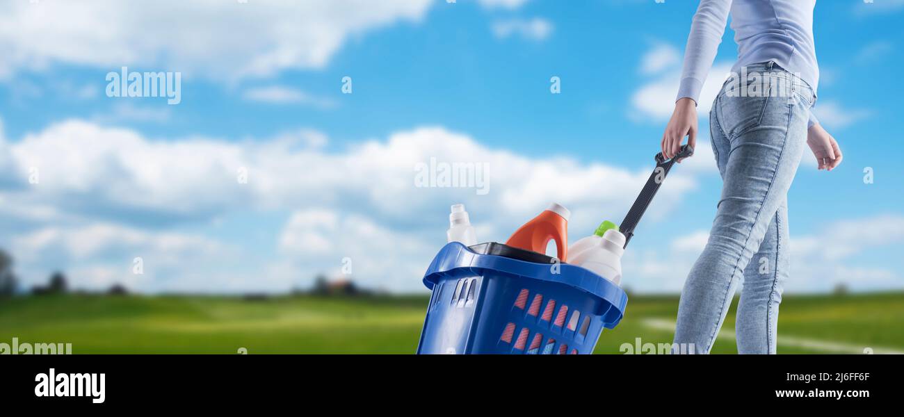 Femme tirant un panier plein de produits de nettoyage et paysage vert dans le fond Banque D'Images