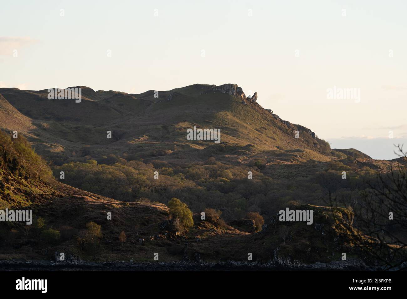 Lumière Golden Hour illuminant les collines escarpées des Highlands écossais et les affleurements rocheux Banque D'Images