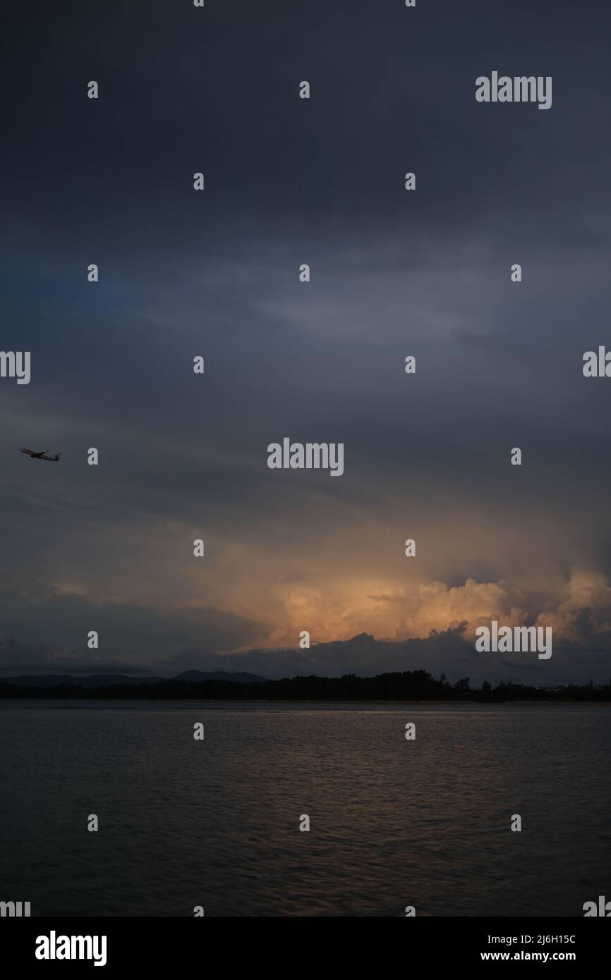 Un avion monte au-dessus de la mer après le décollage, devant un nuage d'orage isolé éclairé par le soleil couchant Banque D'Images