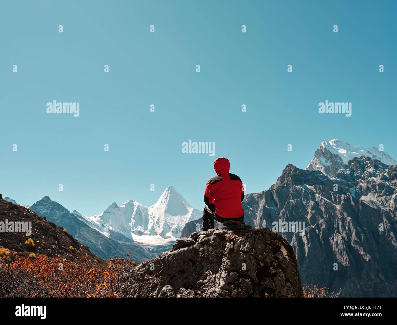 Vue arrière de l'homme asiatique assis au sommet du rocher avec le sommet de la montagne Yangmaiyong (ou Jampayang en tibétain) au loin à Yading, Daocheng County, SIC Banque D'Images