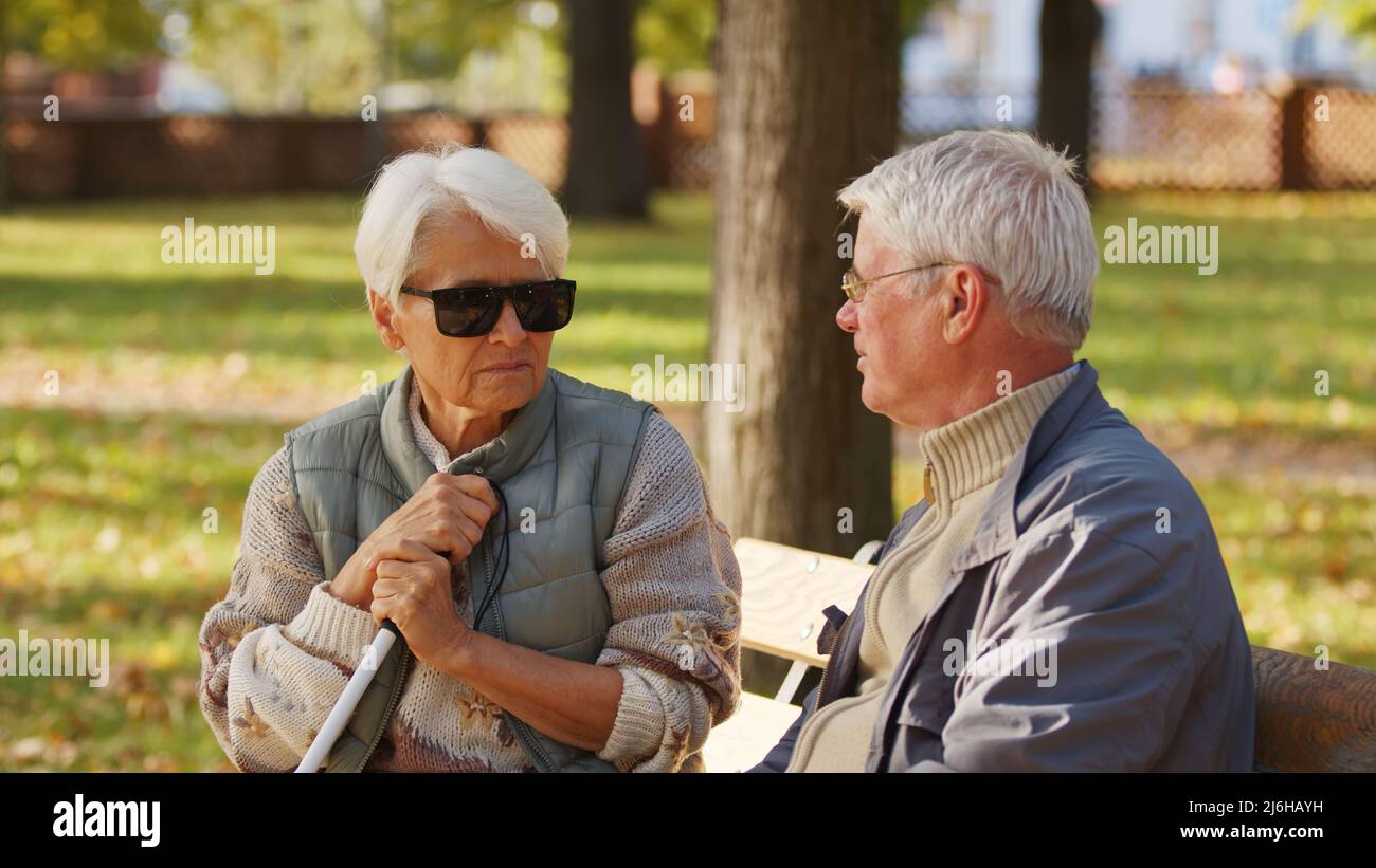 Grands-parents européens retraités à poil gris assis sur un banc dans un  parc en automne. Invalide aveugle caucasienne femme senior avec grue  blanche et lunettes de soleil parle avec son partenaire. Photo